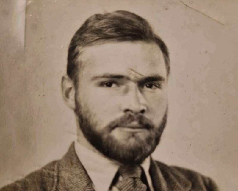 A faded sepia studio portrait of a bearded man in a suit, with a crease running across the forehead and stains across the paper.